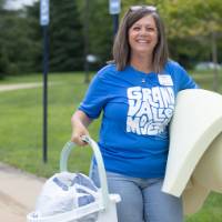 Volunteer smiling at camera while holding mattress pad and laundry bin